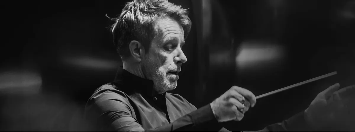A conductor mid-gesture with a baton, in black and white