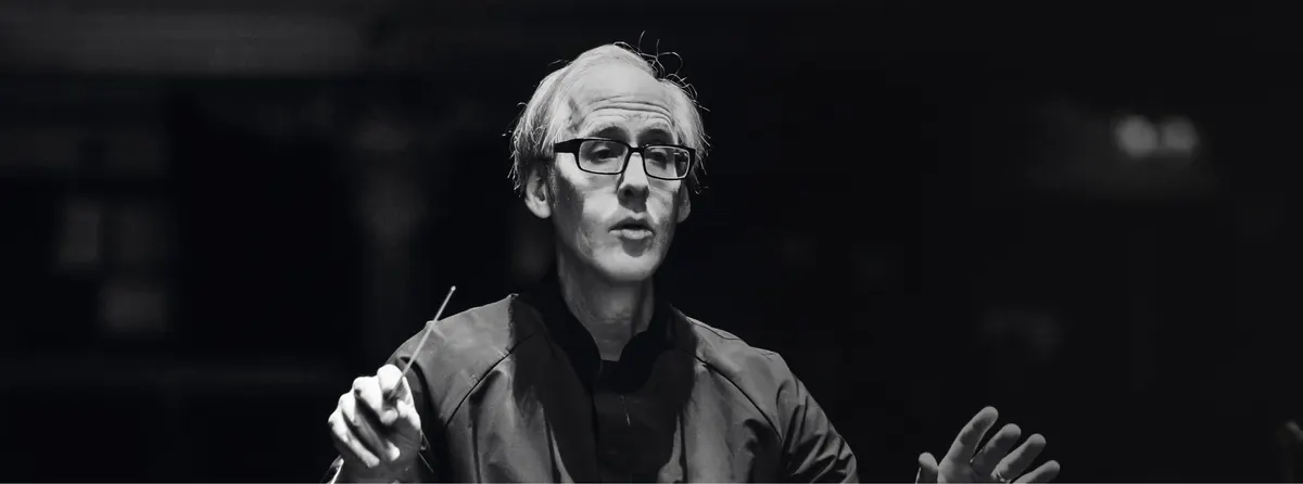 A conductor in glasses leading the orchestra with a baton