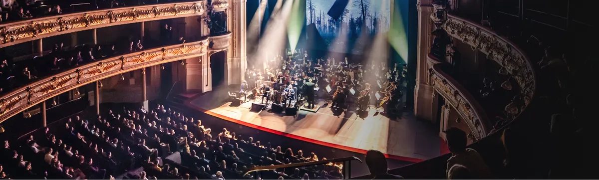 An orchestra on the stage of a historic theatre, seen from the balcony