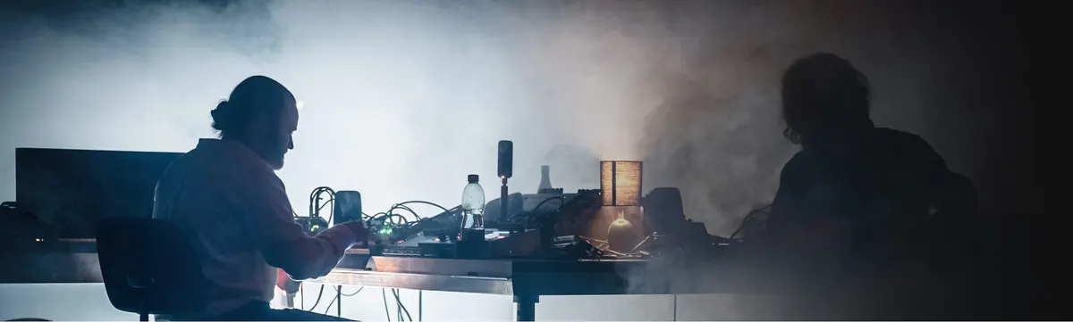 Two musicians at electronic instruments in backlit haze