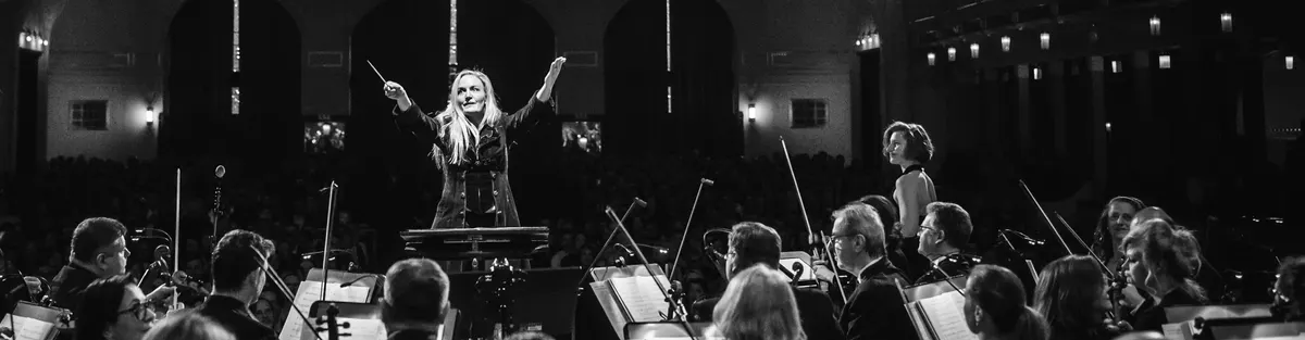 A conductor with arms raised in front of the orchestra and the audience