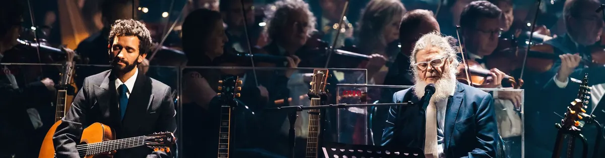 A pianist singing at the piano, a guitarist beside and the orchestra behind