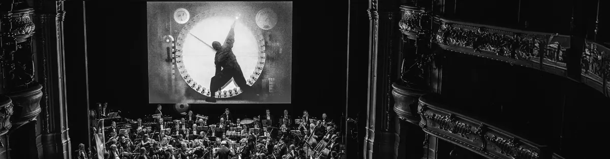 An orchestra playing beneath a silent film projected on a screen
